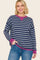 woman wearing a navy blue and white striped long sleeve top with a pink neckline and cuffs, smiling while standing with one hand in her pocket