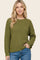 woman wearing an olive green textured knit sweater with long sleeves and a relaxed fit, paired with blue jeans