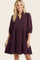 woman wearing a burgundy loose fit tiered dress with three-quarter sleeves and a v-neckline