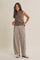 woman wearing a sleeveless brown ribbed sweater and striped wide-leg pants, standing casually with hands in pockets