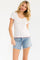 woman wearing a white short sleeve top with red floral print and scalloped edges, paired with denim shorts