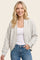 woman wearing a light gray bomber-style cardigan over a white top and blue jeans, smiling at the camera