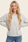 woman wearing a light gray long sleeve henley top with button details and relaxed fit, smiling with hands on hips