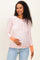 woman wearing a light pink floral maternity top with button details and orange cuffs, holding her baby bump