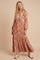 woman wearing a brown patterned maxi dress with long sleeves and a tiered skirt, styled with accessories