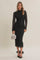 woman wearing a black lace long sleeve midi dress, holding a silver handbag and wearing black heels