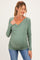 woman wearing a sage green long sleeve maternity top with a wrap design and a visible baby bump
