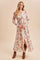 woman wearing a floral maxi dress with long sleeves and a tie waist, paired with brown ankle boots