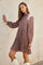 woman wearing a rust floral long sleeve dress with a pleated skirt and standing against a wall