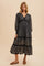 woman wearing a black floral tiered maxi dress with a v-neckline and long sleeves, standing on a neutral background