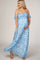 woman wearing a blue floral off-the-shoulder maternity maxi dress and cradling her baby bump