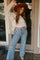woman wearing a light gray oversized sweater and light blue wide-leg jeans, accessorized with a brown wide-brim hat