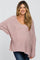 woman wearing a light pink oversized maternity sweater with a scoop neck and long sleeves, showing her baby bump