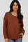 woman wearing a rust-colored oversized sweater with cable-knit sleeves and relaxed fit, paired with blue jeans