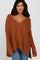 woman wearing an oversized rust cable knit sweater with a deep v-neckline and high-low hem, styled with blue jeans