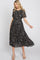 woman wearing a black floral midi dress with short sleeves and a smocked bodice, styled with strappy heels