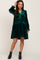woman wearing a dark green velvet tiered mini dress with long sleeves and black ankle boots