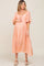 woman wearing a soft peach maternity dress with a tie front and short flutter sleeves, showcasing her baby bump