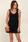 woman wearing a black sleeveless romper with tie-shoulder details and a brown woven crossbody bag
