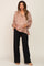 woman wearing a loose beige maternity blouse with a v-neck and black maternity trousers, holding her baby bump