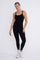 woman wearing a black sleeveless one-piece yoga jumpsuit and white sneakers against a white background