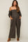woman wearing a dark green strapless maternity jumpsuit with puff sleeves and pockets, showcasing her baby bump