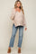woman wearing a light beige knitted maternity sweater with buttons and paired with light wash jeans, showcasing her baby bump