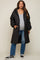 woman wearing a black quilted maternity coat over a gray top and blue jeans, showing her baby bump