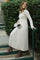 woman wearing a beige long sleeve pleated dress and tan heeled boots, holding a gray clutch, standing on stairs