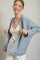 woman wearing a light blue textured cardigan over a white tank top and smiling while holding the cardigan open