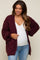 woman wearing a burgundy chunky knit maternity cardigan over a white top and showing her baby bump with blue jeans