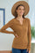 woman wearing a brown long sleeve henley shirt and a wide-brimmed hat, smiling and posing indoors