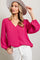 woman wearing a bright pink v-neck blouse with balloon sleeves and white pants, accessorized with a wide-brimmed hat
