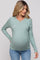 woman wearing a light green ribbed maternity top and showing her baby bump while posing