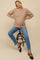 woman wearing a beige cable knit maternity sweater and blue skinny jeans, sitting on a stool with a visible baby bump