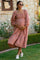 woman wearing a red and white gingham maternity maxi dress, smiling and holding her baby bump in a garden setting