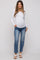 woman wearing a white long sleeve maternity top and blue jeans, showcasing her baby bump