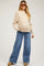 woman wearing a beige ribbed maternity sweater and wide-leg jeans, showing a baby bump and styled with sunglasses