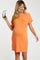 woman wearing an orange short sleeve maternity dress with a pocket, holding sunglasses and showing her baby bump