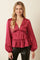 woman wearing a deep burgundy satin long sleeve top with a v-neck and ruffled waist detail