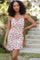 woman wearing a white floral mini dress with a ruffled hem and a thin strap, holding a small woven bag