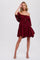 woman wearing a burgundy off-shoulder dress with balloon sleeves and a tiered skirt, posing with one hand raised