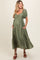 woman wearing a green puff sleeve maternity dress with a tiered skirt and pockets, showing her baby bump