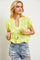 woman wearing a bright yellow knitted cropped cardigan with lace-up detail and distressed denim shorts