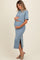 woman wearing a blue maternity crop top and matching skirt, gently cradling her baby bump
