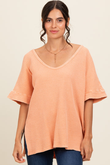 woman wearing a peach-colored loose-fitting top with ruffled sleeves and a v-neckline