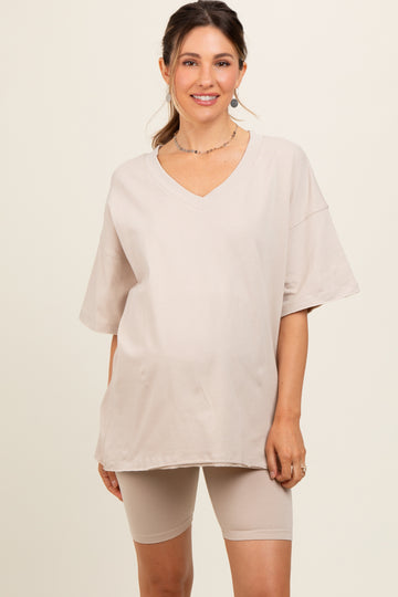 woman wearing a beige oversized v-neck maternity top with matching biker shorts and showing her baby bump