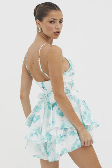 woman wearing a white floral mini dress with ruffles and adjustable spaghetti straps, showing a back view