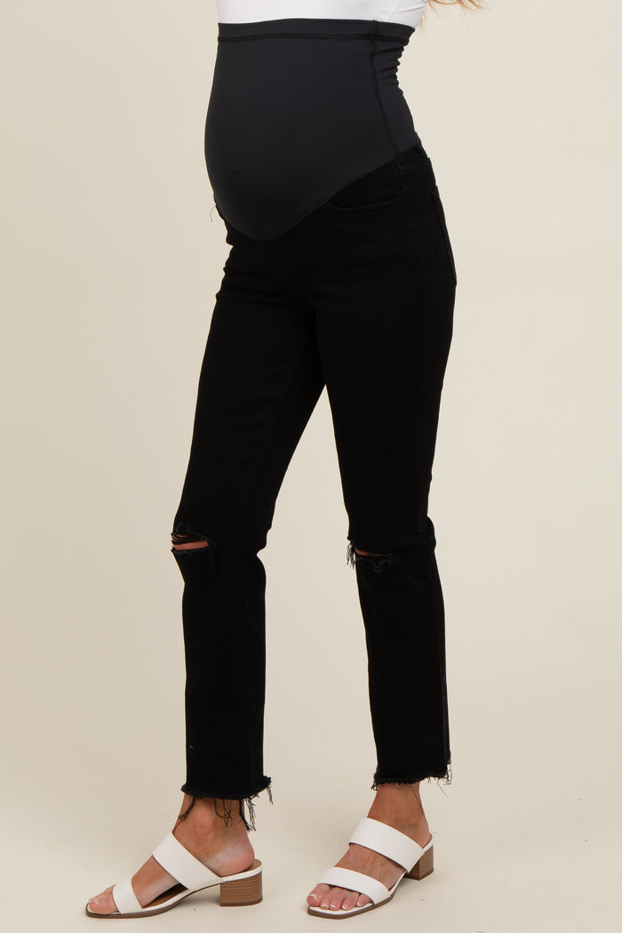 woman wearing black maternity jeans with a distressed hem and a stretchy belly panel, showing her baby bump