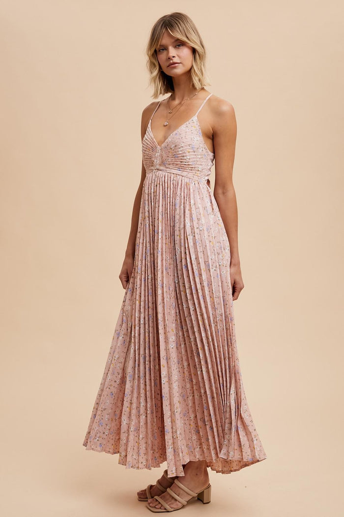 woman wearing a pink floral maxi dress with pleated details and thin straps, standing on a beige background